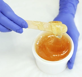 Female hands holding liquid yellow paste sugaring white copy space